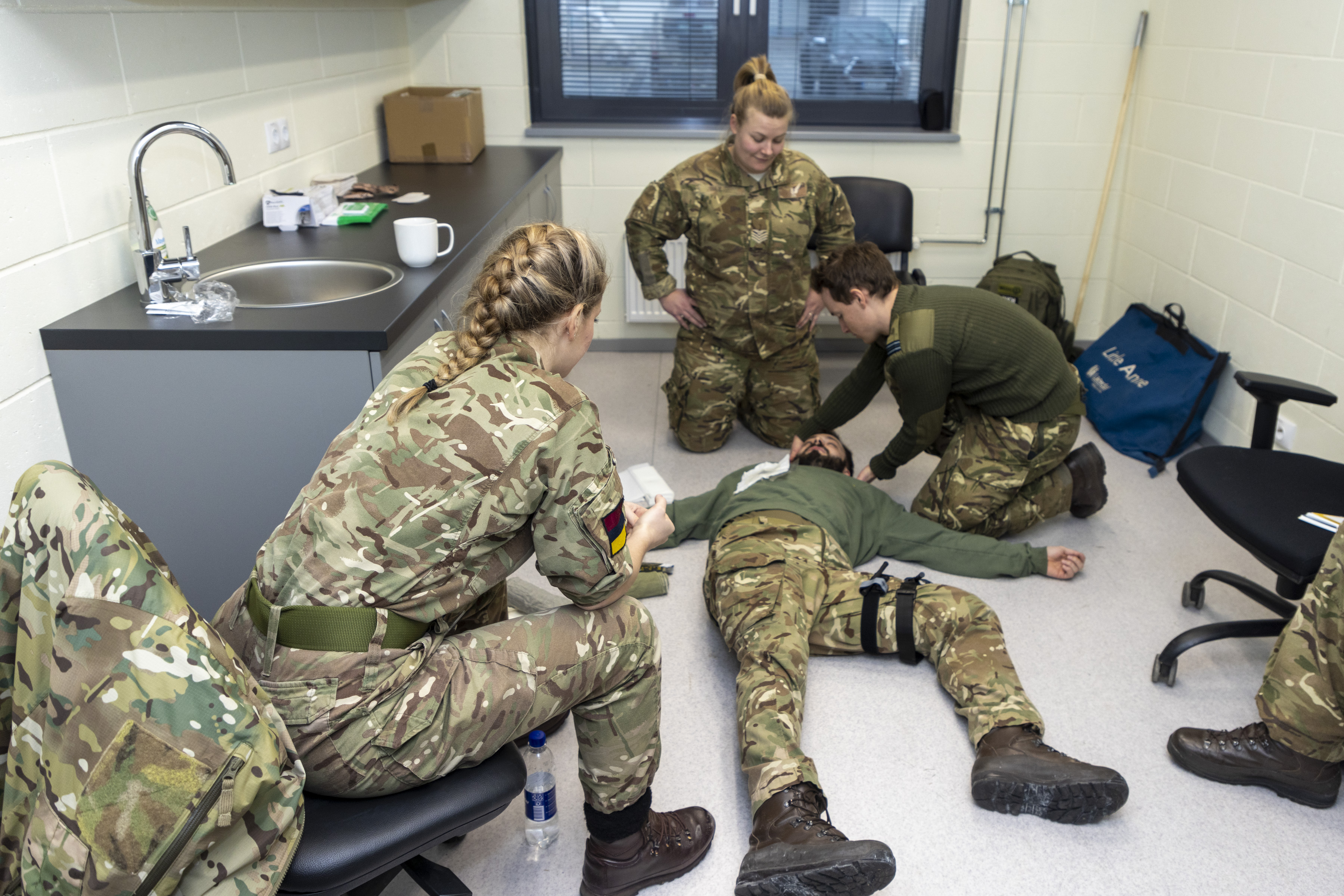 Image shows RAF aviators attending improvised medic scene with patient on the floor in a tea bar. 